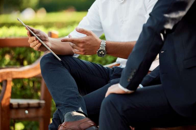 Two people sitting on a bench going through a document on a tablet signifying growth and development. For the RTS Academy "Developing Your People" and "People Development Fundamentals" course.