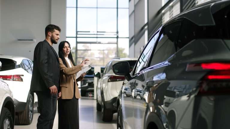 A automotive dealership. Two people are looking at a car. This course focuses on electric vehicles for RTS Academy.
