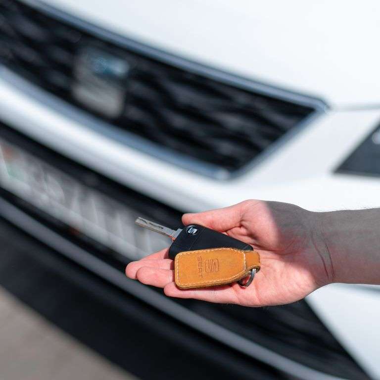 Close-up of a hand holding a car key in front of a white vehicle. Ideal for automotive themes.
