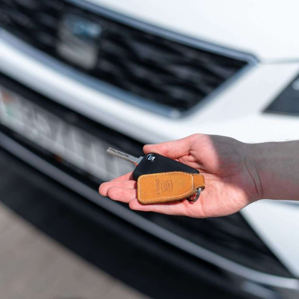 Close-up of a hand holding a car key in front of a white vehicle. Ideal for automotive themes.
