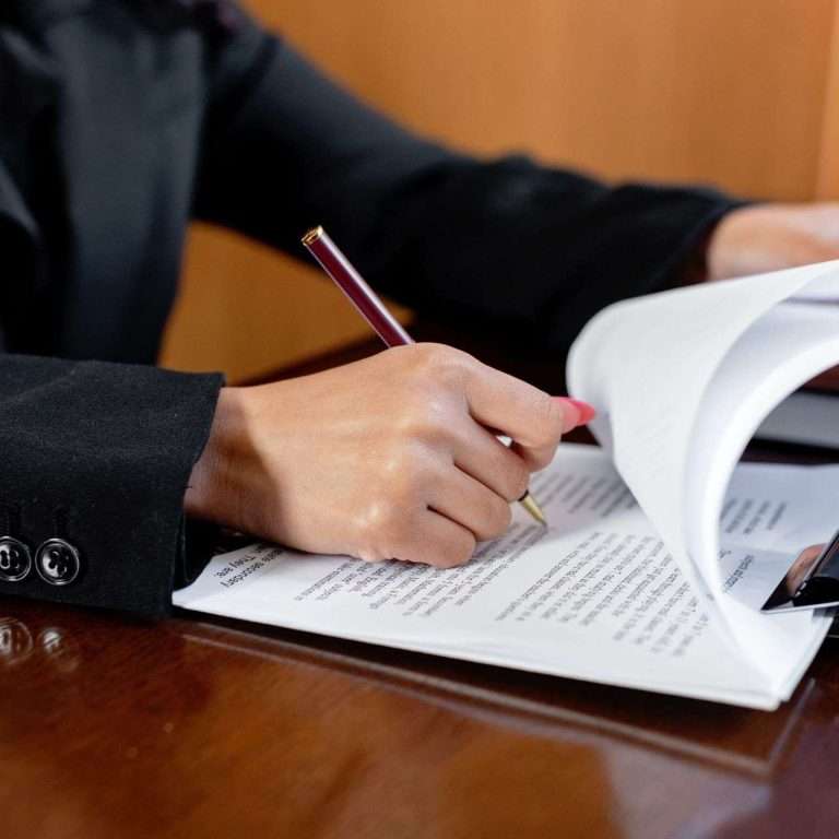 Close-up of a woman signing legal documents with a pen in an office setting.