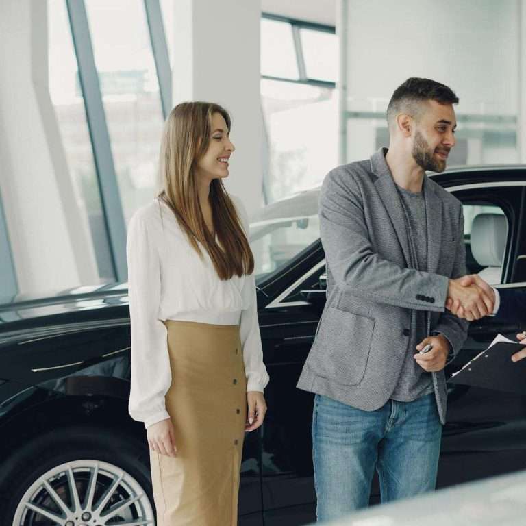 Customers shaking hands with dealer in showroom, sealing car purchase deal.