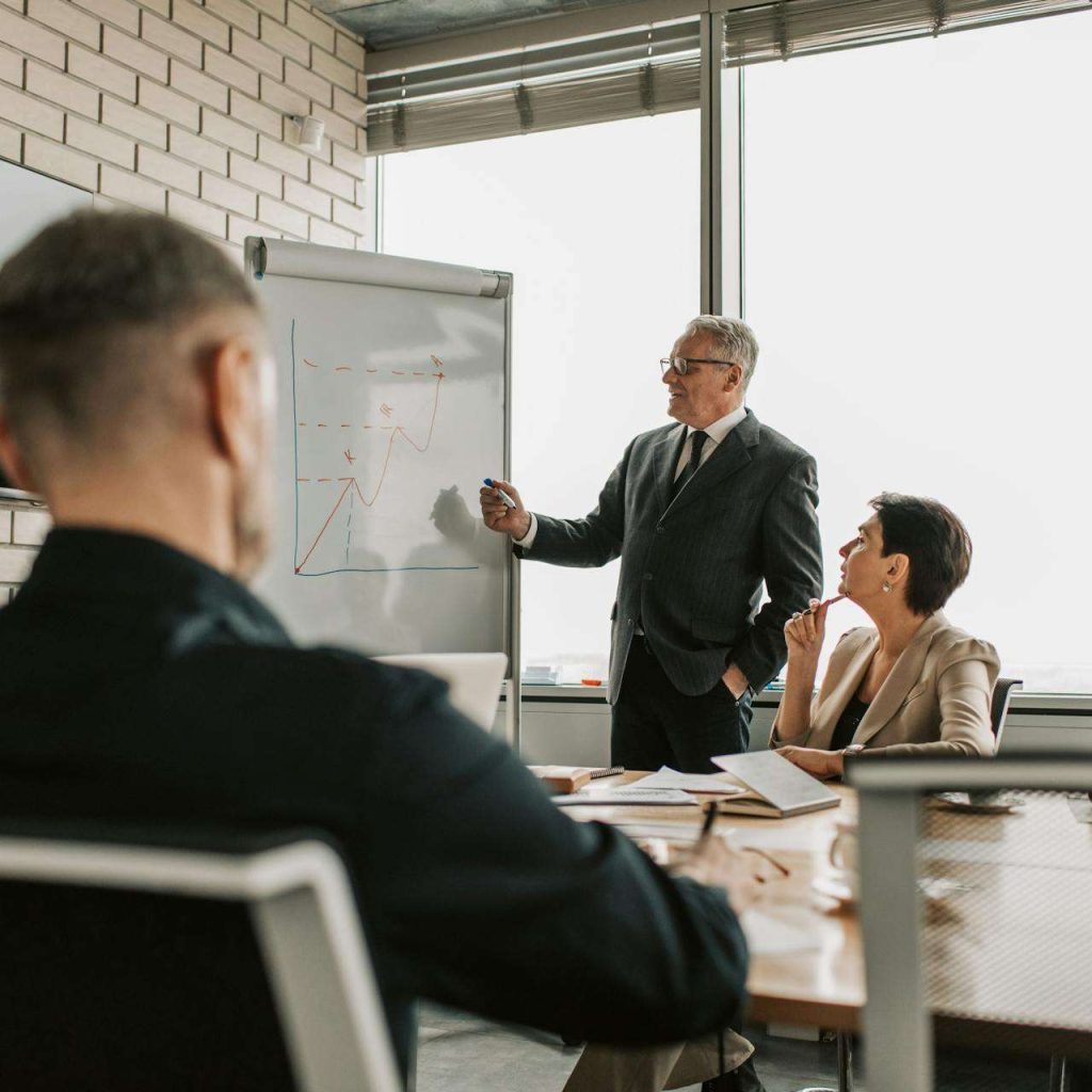 Senior leader presenting growth charts in a business meeting with colleagues in a modern office setting.