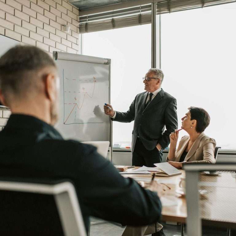 Senior leader presenting growth charts in a business meeting with colleagues in a modern office setting.