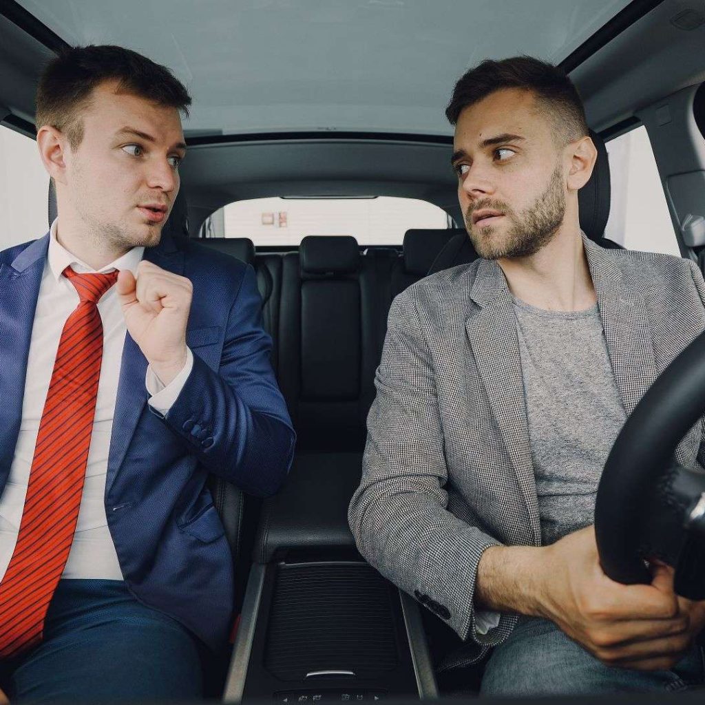 Two businessmen in a car engage in conversation, focusing on discussion details.